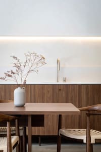 A minimalist residential kitchen with wooden furniture, a white vase with dried flowers, and a modern faucet in the backgroun