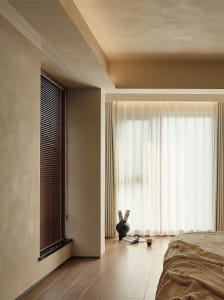 A modern bedroom featuring wooden blinds and sheer curtains