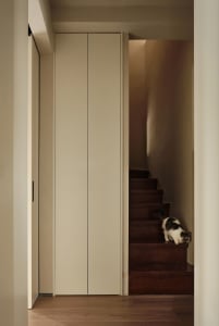 A modern interior design featuring a wooden staircase with a black and white cat sitting on the stairs. The environment is we