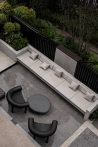 Minimalist outdoor furniture made of concrete, including a long bench with pillows and a small round table.