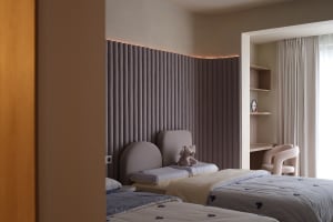 A modern minimalist bedroom with grey curtains, fabric headboards, and light wooden furnishings.