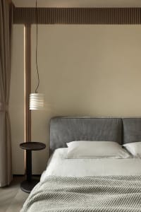 Minimalist bedroom featuring a gray upholstered headboard and textured bedding, set against a beige wall and floor with ambie