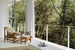 Modern living room with white marble floor and white textured walls, featuring contemporary furniture and a view of lush gree