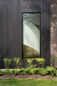 A modern building with black wooden exterior and green plants in front of it.