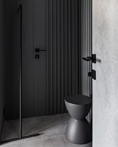 Modern minimalist bathroom featuring a sleek, black toilet and a textured concrete floor.