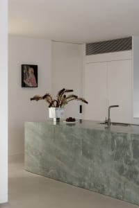 A modern kitchen with a marble countertop featuring a vase of flowers and a plate of fruit.