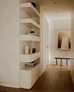 A modern minimalist living room with sleek, white shelves, wooden flooring, and a black bench with a framed abstract artwork.