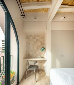 A minimalist bedroom featuring a white bed with a green lamp and a wooden floor.