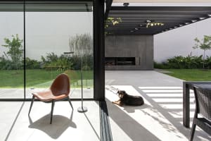 A modern patio with concrete flooring and a brown leather chair, featuring a dog lying on the ground and a grill area.