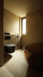 A modern bathroom with tiled walls and floor, featuring a sleek black toilet, a freestanding bowl-shaped bathtub with a metal