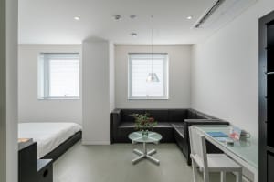 A minimalistic modern studio apartment with metallic accents and a fabric sofa, featuring a glass table and white walls.