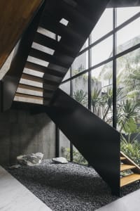 Modern industrial steel staircase with concrete floor, surrounded by large glass windows and greenery.