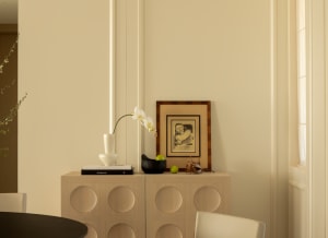 A minimalist interior design featuring a wooden cabinet with circular cutouts, placed beneath a window with natural light str