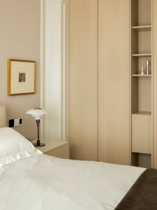 A modern bedroom with a neatly made bed, a nightstand with a white lamp, and a framed picture on the wall.