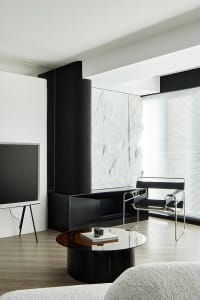 A modern living room featuring black and white decor, with a metal fireplace, glass table, and minimalist furnishings.