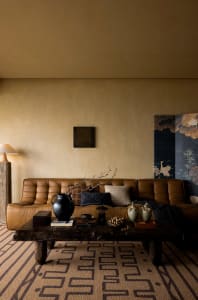 A modern living room featuring a brown leather sofa, a wooden table with decorative items, and a floor lamp in the corner.