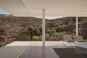 Interior of a modern residential space featuring large glass windows with a scenic view of hills and vegetation.