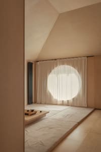 A minimalist living room featuring wooden furniture and a round window.
