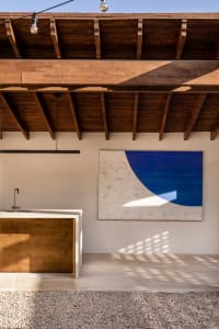 Minimalist interior design with wooden ceiling beams and a blue abstract painting.