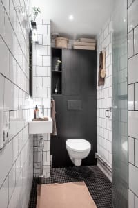 A minimalist bathroom with black and white tiles, featuring a sink, toilet, and shower.