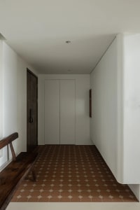 A minimalist entryway featuring a tiled floor and wooden bench against white walls.