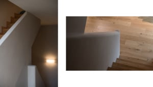 A minimalist staircase made of wood, with a warm light fixture mounted on the wall.