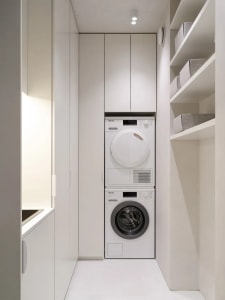 A minimalist laundry room with a white cabinet, washing machine, dryer, and organized shelves.