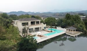 A modern poolhouse with a large outdoor swimming pool, surrounded by lush greenery and overlooking a serene lake.