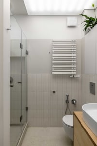 A minimalist bathroom with white tiles and a glass shower enclosure.
