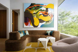 A modern living room with a curved couch, colorful abstract painting, and geometric coffee tables.
