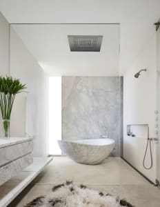 Modern minimalist bathroom with a freestanding marble tub, white walls, and a white marble pedestal sink.