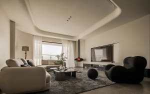 Contemporary living room featuring neutral-toned fabrics and tiles, a black rocking chair, and a suspended fireplace.