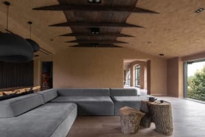 A modern living room with concrete walls, a grey sectional sofa, and wooden tree stump stools.