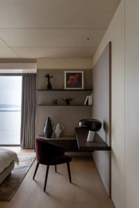 A modern minimalist bedroom featuring a wooden desk, chair, and shelves with decorative items.