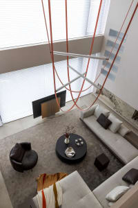 A modern living room with a large window, upholstered furniture, and a hanging art installation.