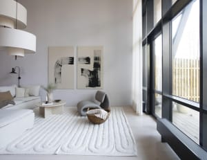 A modern minimalist living room with white walls, a grey lounge chair, and a white rug with an abstract design.
