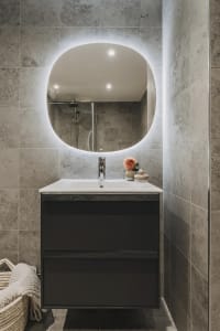 A minimalist bathroom with a modern industrial design featuring concrete tiles and a circular mirror with LED lighting.