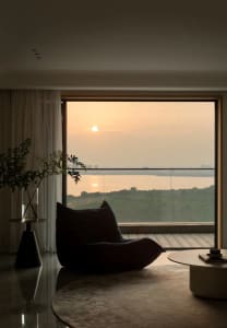 A modern living room with a large glass window showcasing a scenic sunset view.