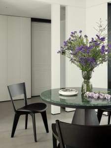 A modern dining room featuring a green marble table with a vase of purple flowers and black chairs.