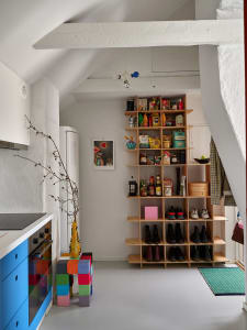 A minimalist kitchen features a tall wooden shelf stocked with various food and kitchen items, a colorful block storage unit,