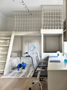 A modern loft bedroom featuring a loft bed surrounded by a net, a built-in desk area with office chairs, and a cozy seating a