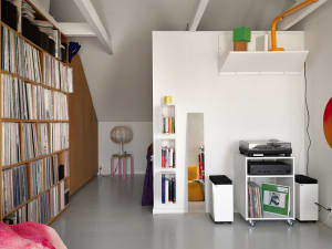 A minimalist living room with white floor, walls, and ceiling, featuring white glass shelving units, a yellow chair, and a co
