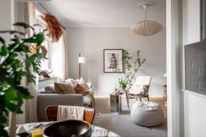 A cozy living room with a neutral-toned sofa, armchair, and coffee table, decorated with plants and a framed picture.