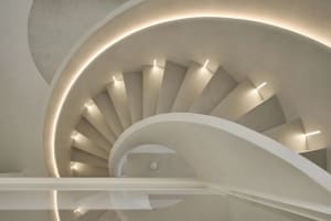 Circular modern staircase with concrete steps, illuminated by warm lighting fixtures.