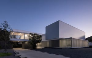 A modern residential building with glass walls, concrete exterior, and metallic elements.