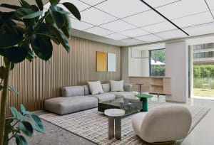 A minimalist living room with concrete and glass elements, featuring a modern sofa, coffee table, and a green stool.