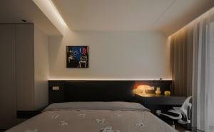 Contemporary bedroom with a black bed frame and white textiles, featuring a modern abstract painting and warm ambient lightin
