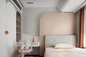 Minimalist children's room with white and beige furniture, a pink chair, and neutral color palette.