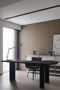 A minimalist office workspace with a wooden desk and chair, featuring a desk lamp and various items on the desk in a well-lit