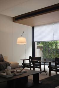 A modern indoor living room with wooden furniture and a large window, illuminated by a white floor lamp.